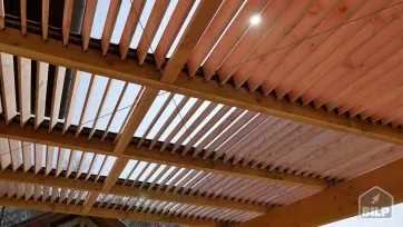 Structure en bois avec des lattes laissant passer la lumière, créant un jeu d’ombre et de lumière sous un auvent.