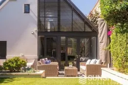 Jardin moderne avec une belle terrasse, des meubles confortables et une façade vitrée, idéal pour se détendre en plein air.