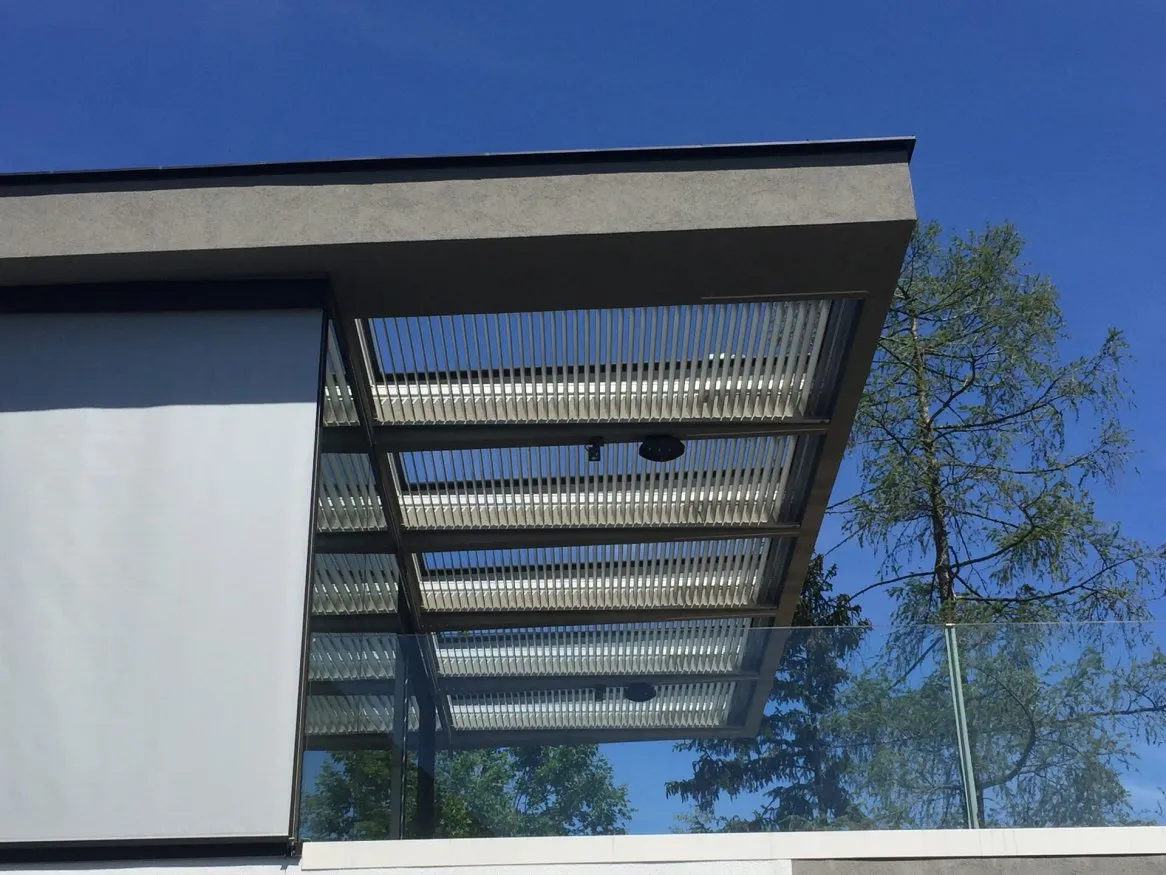Toit moderne en verre et métal avec brise-soleil, sur fond de ciel bleu et feuillage verdoyant. Parfait pour l’architecture contemporaine.
