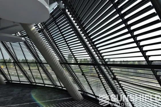 Intérieur moderne d’un bâtiment avec de grandes fenêtres et des volets inclinables, offrant une vue lumineuse et aérée.