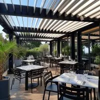 Terrasse de restaurant moderne avec tables élégantes, pergola, verdure et vue sur l’extérieur, idéale pour un repas en plein air.