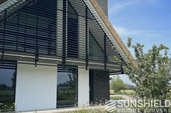 Maison moderne avec toit en pente, façade en blancs et noirs, et volets à lames, entourée de verdure et de paysage.