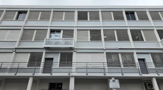 Façade d’un bâtiment moderne avec volets horizontaux, balcons et fenêtre, dans un style architectural contemporain.