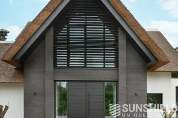 Façade moderne d’une maison avec toit en chaume et grandes fenêtres, alliant design contemporain et nature.